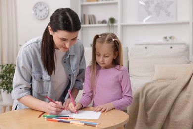 Photo of Mother teaching her daughter to draw at table indoors, space for text