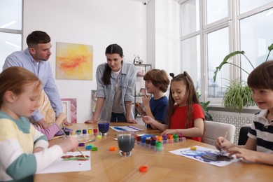 Photo of Kids with teachers at painting lesson indoors. Learning to draw