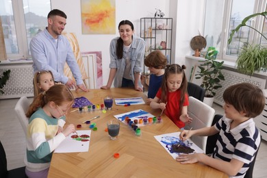 Photo of Kids with teachers at painting lesson indoors. Learning to draw