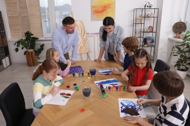 Photo of Kids with teachers at painting lesson indoors. Learning to draw