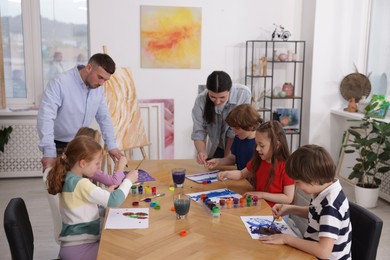 Photo of Kids with teachers at painting lesson indoors. Learning to draw