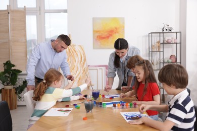 Photo of Kids with teachers at painting lesson indoors. Learning to draw