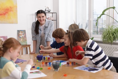 Photo of Woman teaching kids to draw at painting lesson indoors