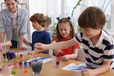 Photo of Woman teaching kids to draw at painting lesson indoors