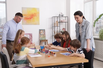 Photo of Kids with teachers at painting lesson indoors. Learning to draw