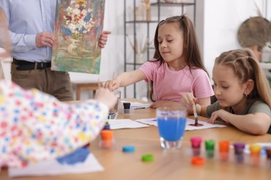 Photo of Kids with teacher at painting lesson indoors. Learning to draw