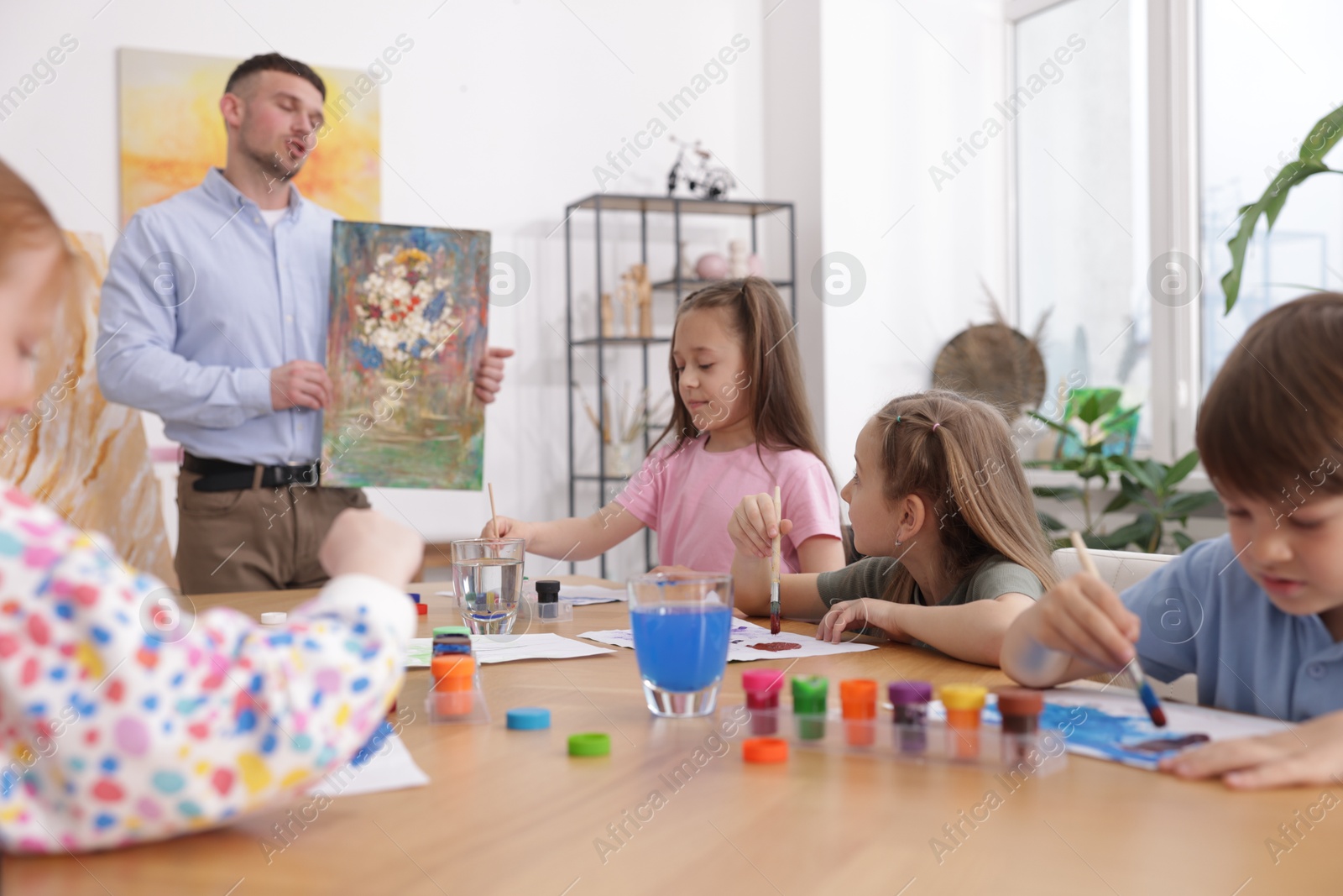 Kids with teacher at painting lesson indoors, selective focus. Learning to draw Photo of Kids with teacher at painting lesson indoors, selective focus. Learning to draw