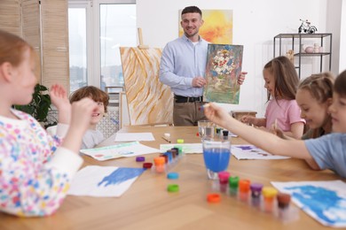 Photo of Kids with teacher at painting lesson indoors. Learning to draw