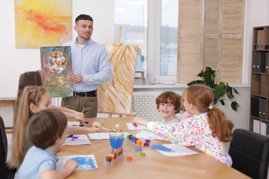 Photo of Kids with teacher at painting lesson indoors. Learning to draw