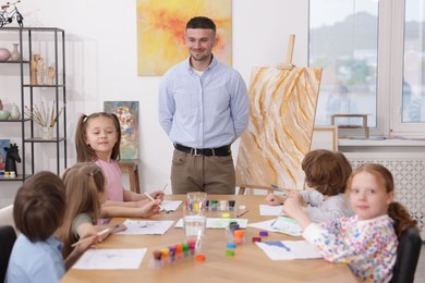 Photo of Man teaching kids to draw at painting lesson indoors