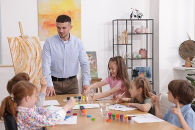 Photo of Man teaching kids to draw at painting lesson indoors