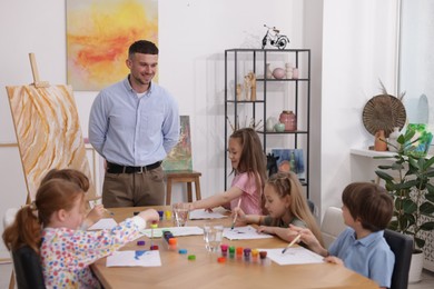 Photo of Man teaching kids to draw at painting lesson indoors