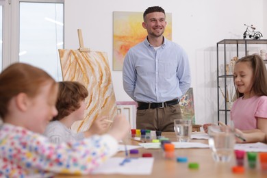 Photo of Man teaching kids to draw at painting lesson indoors
