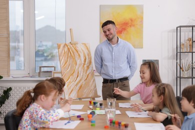 Photo of Man teaching kids to draw at painting lesson indoors