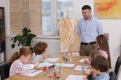 Photo of Man teaching kids to draw at painting lesson indoors
