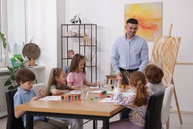 Photo of Man teaching kids to draw at painting lesson indoors