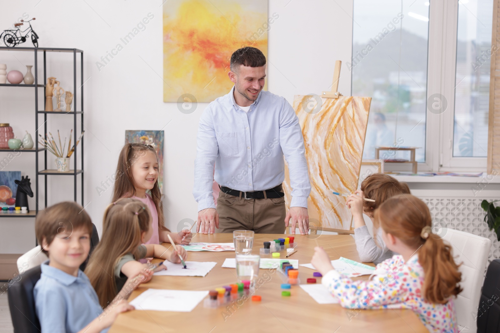 Man teaching kids to draw at painting lesson indoors Photo of Man teaching kids to draw at painting lesson indoors