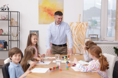 Photo of Man teaching kids to draw at painting lesson indoors