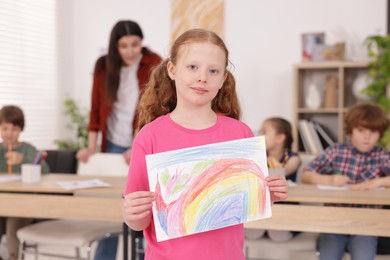 Photo of Cute girl showing her drawing during painting lesson indoors, selective focus
