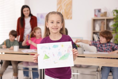 Photo of Cute girl showing her drawing during painting lesson indoors, selective focus