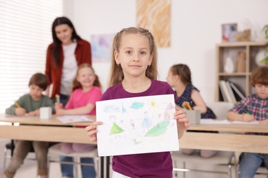Photo of Cute girl showing her drawing during painting lesson indoors, selective focus