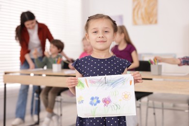 Photo of Cute girl showing her drawing during painting lesson indoors, selective focus
