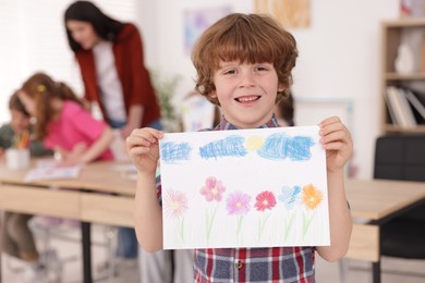 Photo of Cute boy showing his drawing during painting lesson indoors, selective focus