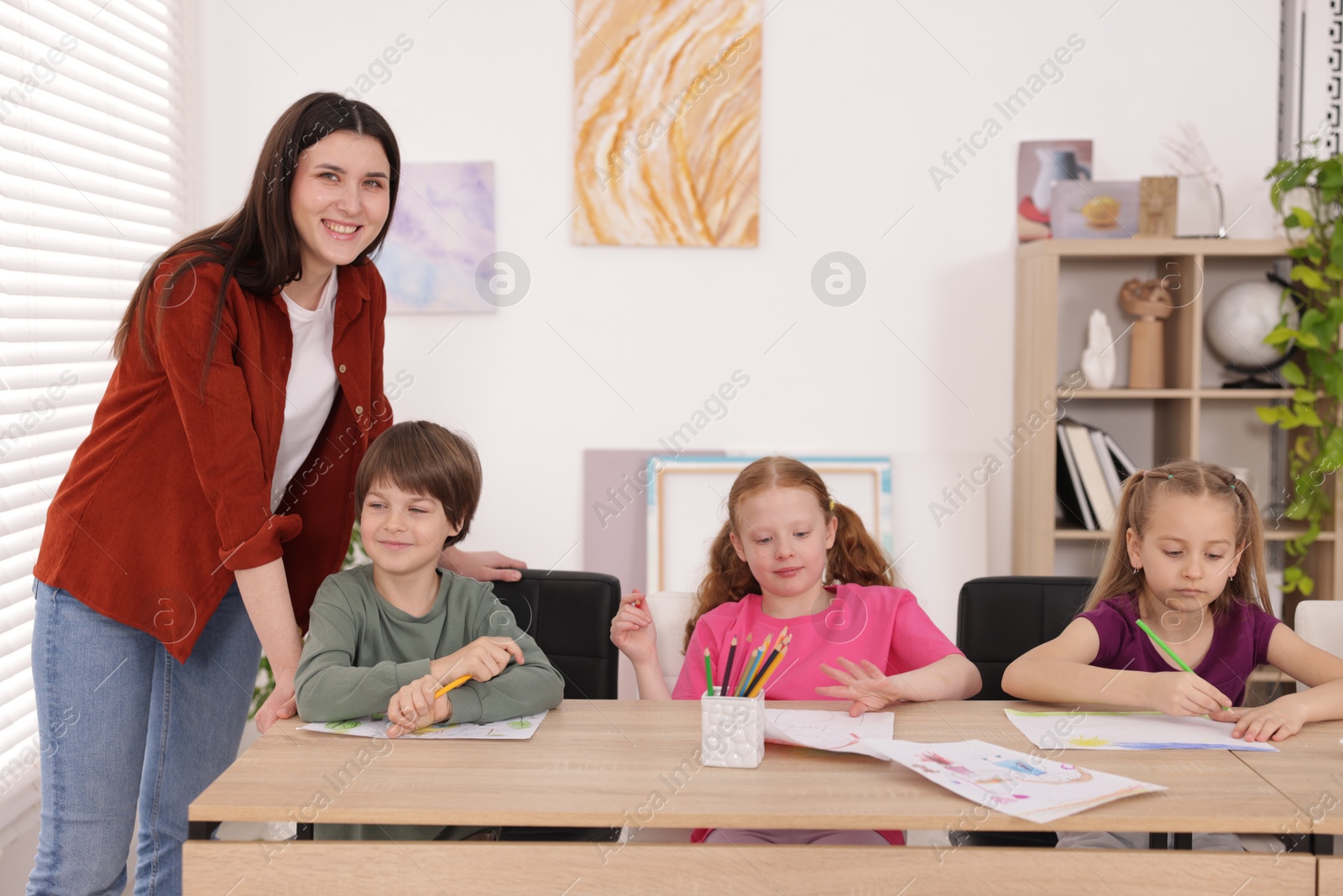Woman teaching kids to draw at painting lesson indoors Photo of Woman teaching kids to draw at painting lesson indoors