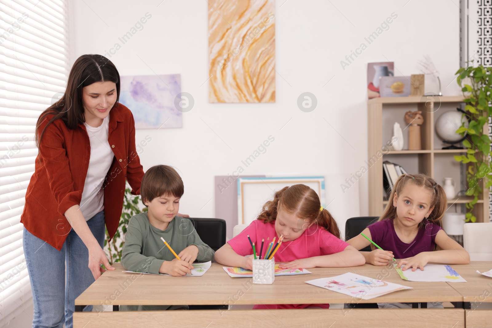 Woman teaching kids to draw at painting lesson indoors Photo of Woman teaching kids to draw at painting lesson indoors