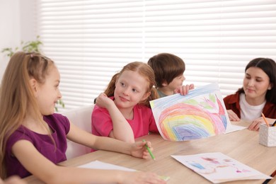 Photo of Woman teaching kids to draw at painting lesson indoors