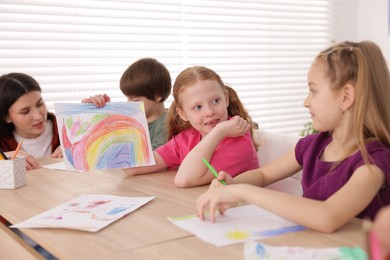 Photo of Woman teaching kids to draw at painting lesson indoors