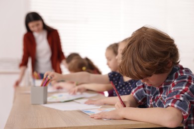 Photo of Woman teaching kids to draw at painting lesson indoors, selective focus