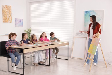 Photo of Woman teaching kids to draw at painting lesson indoors