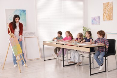 Photo of Woman teaching kids to draw at painting lesson indoors