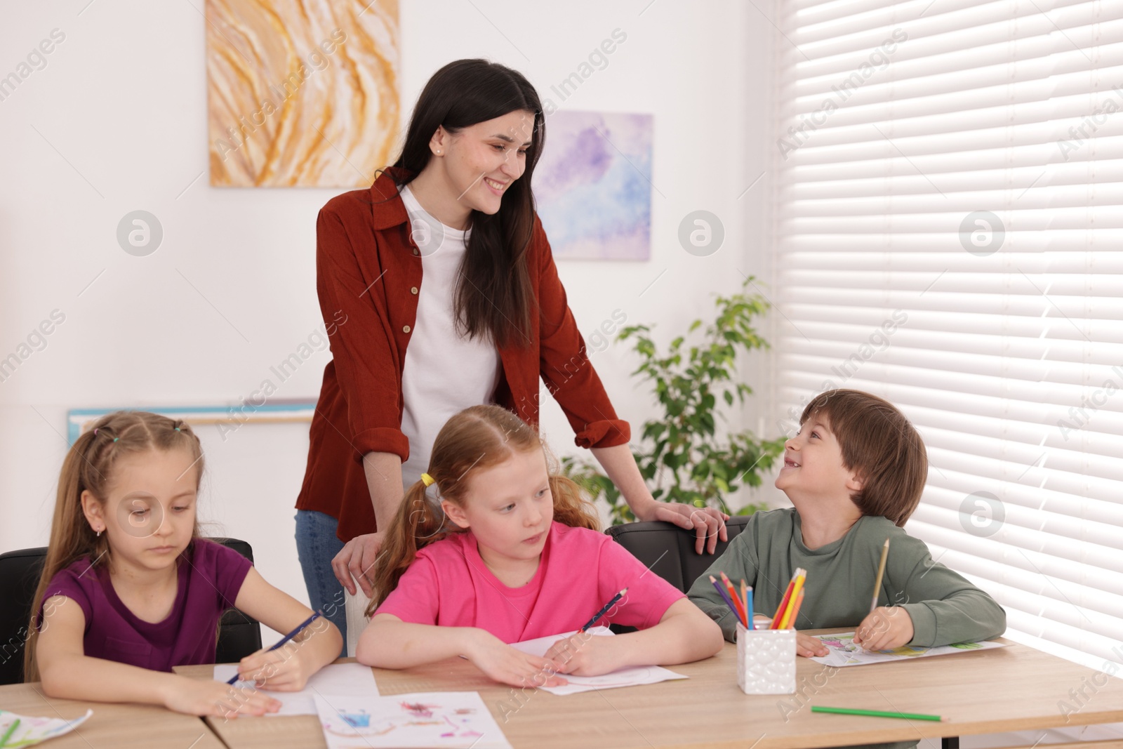 Woman teaching kids to draw at painting lesson indoors Photo of Woman teaching kids to draw at painting lesson indoors