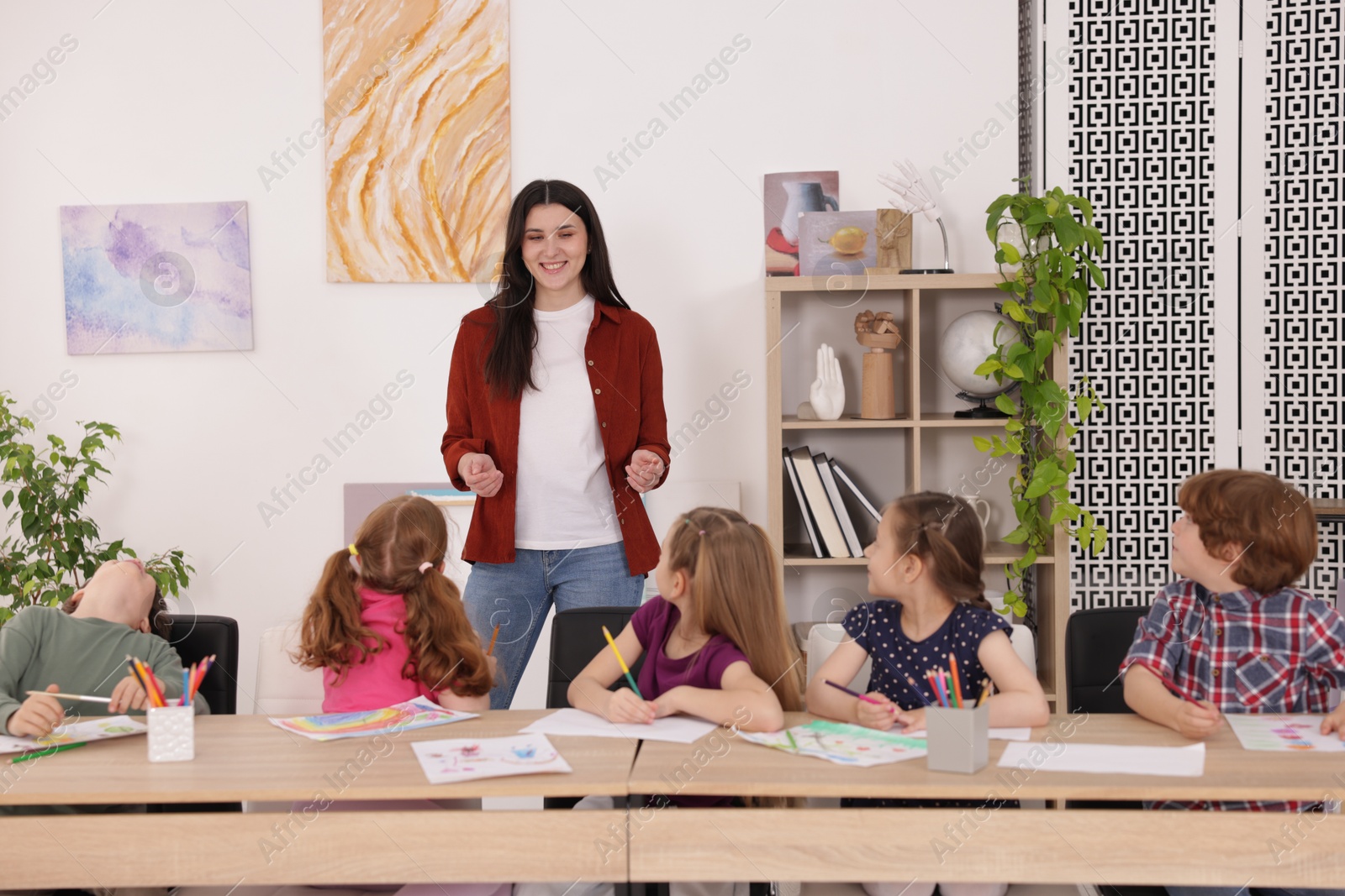 Woman teaching kids to draw at painting lesson indoors Photo of Woman teaching kids to draw at painting lesson indoors