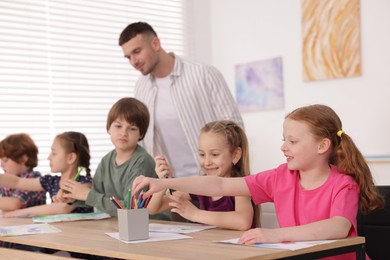 Photo of Man teaching kids to draw at painting lesson indoors, selective focus