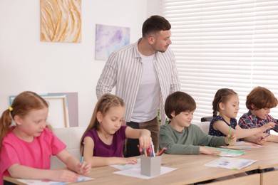 Photo of Man teaching kids to draw at painting lesson indoors