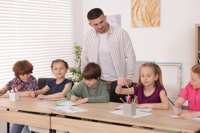 Photo of Man teaching kids to draw at painting lesson indoors