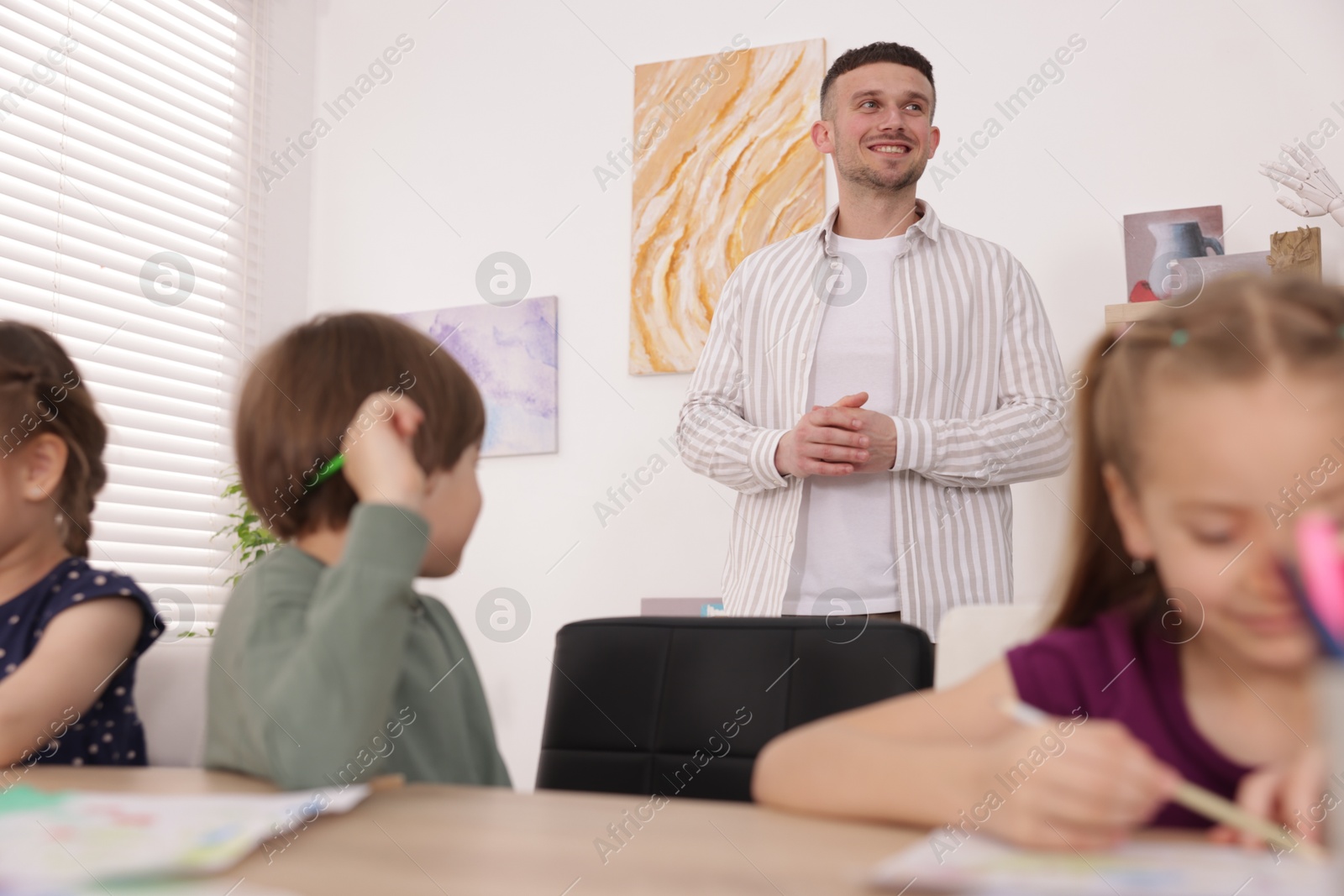Man teaching kids to draw at painting lesson indoors, selective focus Photo of Man teaching kids to draw at painting lesson indoors, selective focus