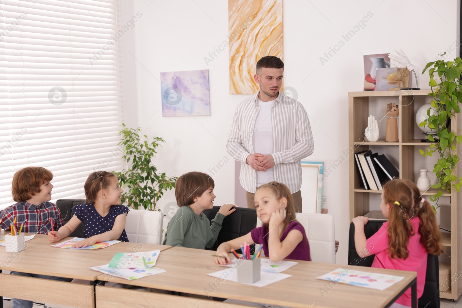 Man teaching kids to draw at painting lesson indoors Photo of Man teaching kids to draw at painting lesson indoors