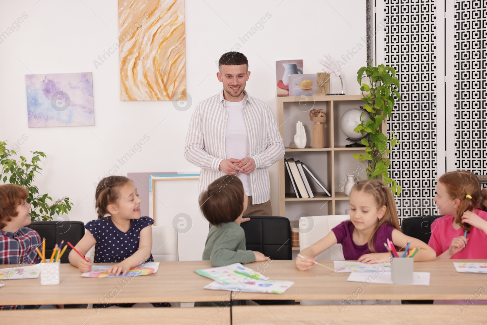 Man teaching kids to draw at painting lesson indoors Photo of Man teaching kids to draw at painting lesson indoors