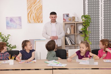 Photo of Man teaching kids to draw at painting lesson indoors