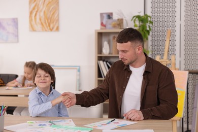 Photo of Man teaching kid to draw at painting lesson indoors, selective focus