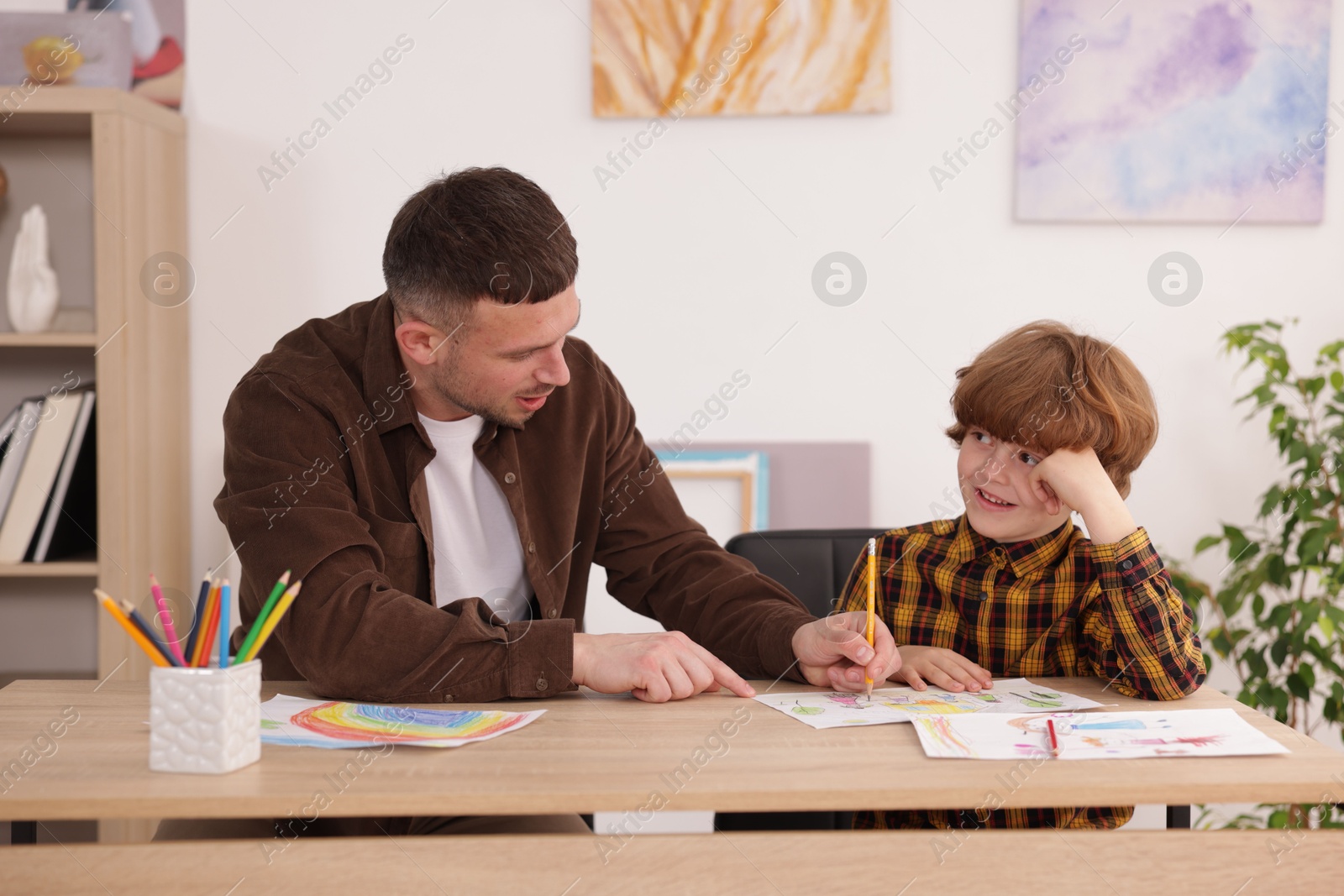 Man teaching kid to draw at painting lesson indoors Photo of Man teaching kid to draw at painting lesson indoors
