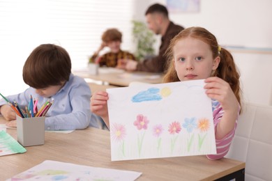 Photo of Cute girl showing her drawing during painting lesson indoors, selective focus