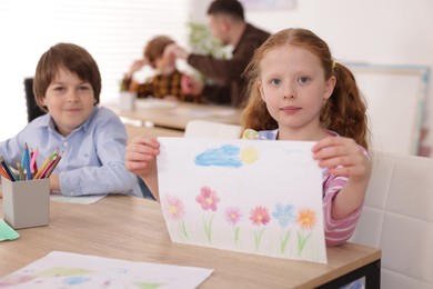 Photo of Cute girl showing her drawing during painting lesson indoors, selective focus