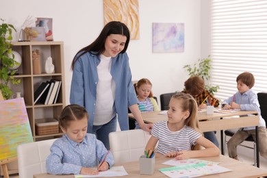 Photo of Woman teaching kids to draw at painting lesson indoors, selective focus