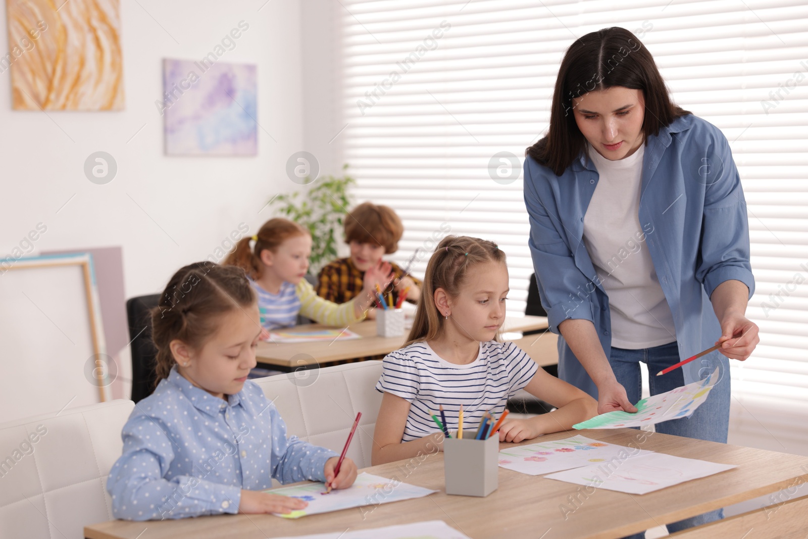 Woman teaching kids to draw at painting lesson indoors, selective focus Photo of Woman teaching kids to draw at painting lesson indoors, selective focus