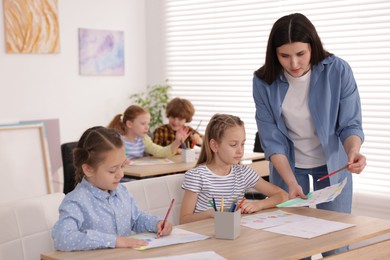 Photo of Woman teaching kids to draw at painting lesson indoors, selective focus